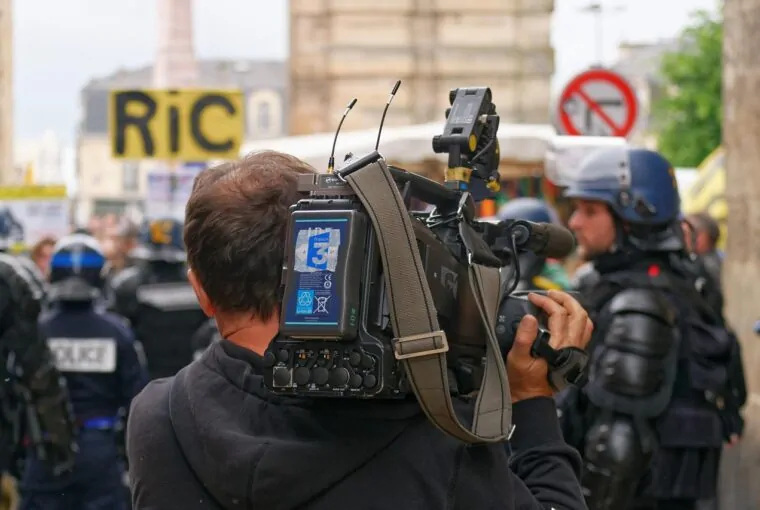 Cinegrafista em protesto com policiais ao fundo - cobertura livre de manifestações é uma das ameaças a jornalistas listadas pela ONU
