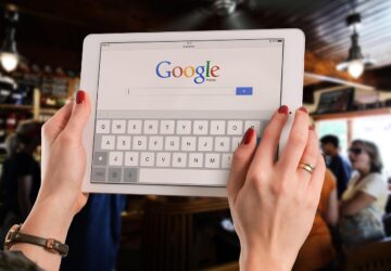 Mãos segurando um tablet com a página de busca do Google aberta, ilustrando o contexto da queixa antitruste contra o Google por uso de IA nos resultados de busca