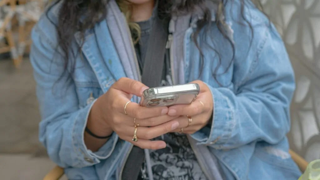 Jovem com roupa jeans e telefone celular nas mãos