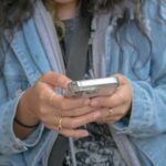 Jovem com roupa jeans e telefone celular nas mãos