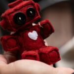Mão segurando robô vermelho de inteligência artificial com coração