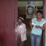 Mulher na porta de um bar em Cuba olhando o celular e com crianças ao lado