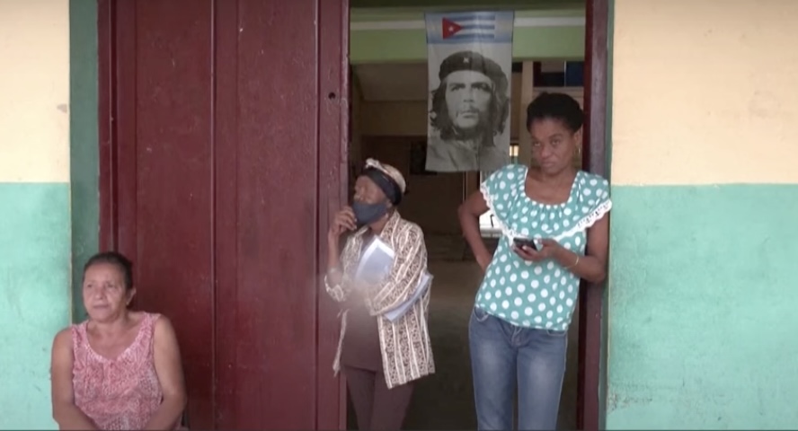 Mulher na porta de um bar em Cuba olhando o celular e com crianças ao lado