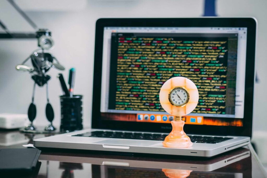 Computador com linhas de código na tela e relógio antigo em primeiro plano