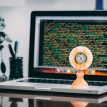Computador com linhas de código na tela e relógio antigo em primeiro plano