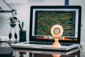 Computador com linhas de código na tela e relógio antigo em primeiro plano