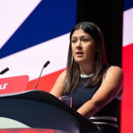 Lisa Nandy, secretária de cultura do Reino Unido com bandeira ao fundo