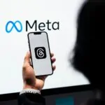 pessoa com smartphone mostrando logo do Instagram e ao fundo a logomarca da Meta