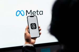 pessoa com smartphone mostrando logo do Instagram e ao fundo a logomarca da Meta
