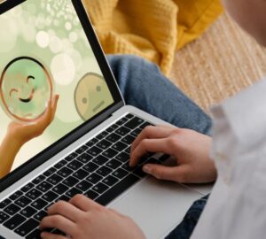 Jovem no computador com tela mostrando emoji feliz, ilustrando reportagem sobre representação de suicídio e saúde mental no Setembro Amarelo